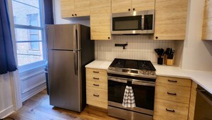 A kitchen with wooden cabinets, stainless steel appliances, and a window with curtains.