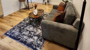 A modern living room with a grey sofa, a round coffee table, a floor lamp, a large mirror, and a TV mounted on the wall.