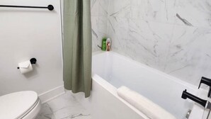 A bathroom with a toilet, a shower with a green curtain, and a marble wall.