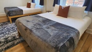 A modern hotel room with two beds, a large window, and a view of buildings outside.