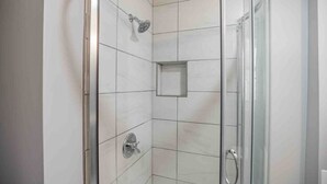 Une douche fermée par des parois en verre, dotée d’un pommeau de douche à main et de commandes fixées au mur.