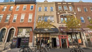 Une rangée d’immeubles en briques avec des devantures de magasins, dont un restaurant de cuisine thaïlandaise et un bar à sushis.