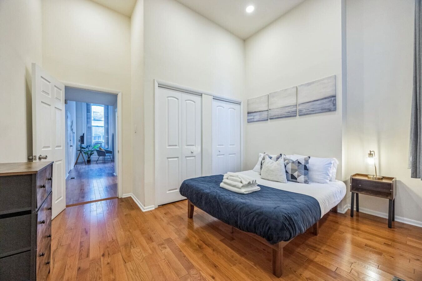 Une chambre avec un lit, un bureau et une armoire. Un couloir mène à une autre pièce.