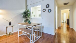 A spacious room with wooden flooring, a glass-top table with a bench, a potted plant, and wall-mounted decorative mirrors.