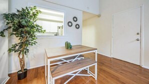 A room with a wooden floor, a white door, a window, a plant, and a table with a mirror and decorative items.
