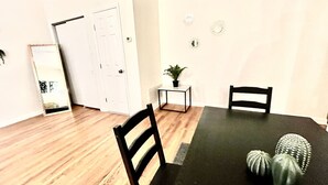 Un coin repas avec une table noire, deux chaises, une petite table d’appoint avec une plante, et une porte visible au fond.