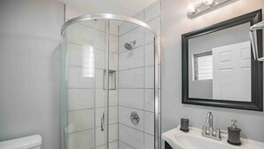 Une salle de bain moderne avec une douche à parois de verre, un lavabo blanc avec un miroir et des toilettes.