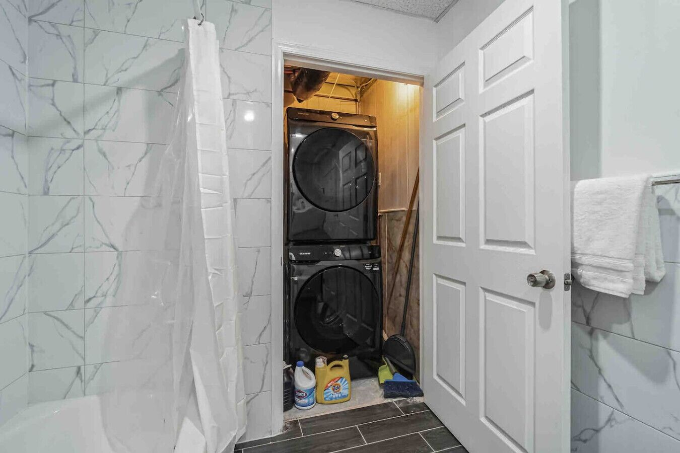 A laundry room with two stacked washing machines, a white door, and a towel hanging on the wall.