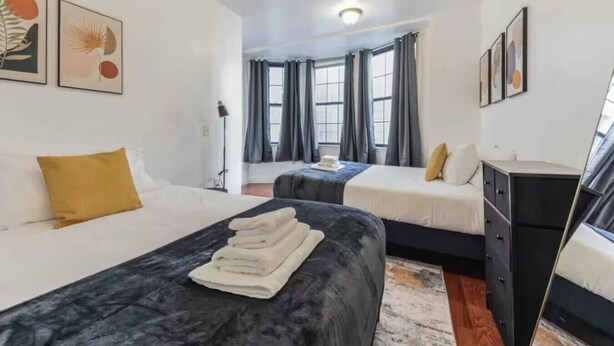 A hotel room with two beds, a desk, and a dresser. There are curtains on the windows, and artwork on the walls. - Across from Convention Center | Sleeps 6 | 3F (Philadelphia)