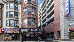 A street view with a corner building, a sushi restaurant, and a parking garage.
