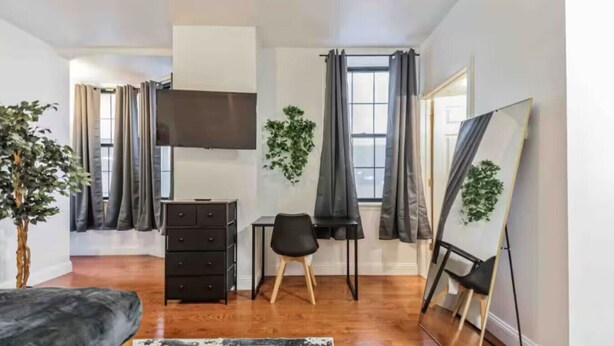 A modern room with a bed, a desk, a chair, a TV, and a large mirror.