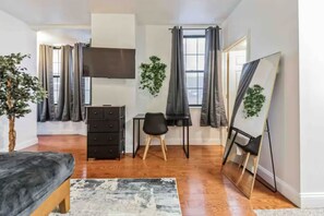 A modern room with a bed, a desk, a chair, a TV, and a large mirror. - Cozy Studio across from Convention Center | 4R (Philadelphia)