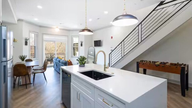 Una cocina moderna con una isla central, un área de comedor con sofá y una escalera que sube a un nivel superior.