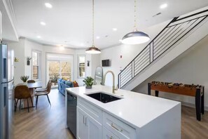 A modern kitchen with a central island, a dining area with a sofa, and a staircase leading to an upper level.