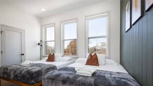 Habitación de hotel con dos camas, ventanas amplias, una puerta y un cuadro en la pared.