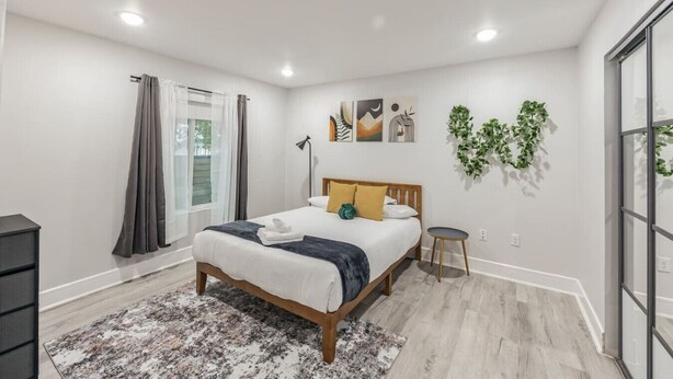 Un dormitorio moderno con cama, mesita de noche, lámpara de pie y ventana con cortinas.