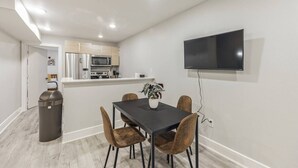 Una cocina moderna con electrodomésticos de acero inoxidable, un comedor con mesa negra y sillas de madera, y un televisor de pantalla plana montado en la pared.