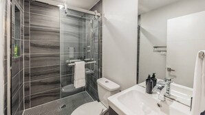 Un baño moderno con ducha de vidrio, inodoro, lavamanos y espejo.