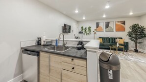 Una cocina moderna con lavavajillas, fregadero y licuadora. Hay un sofá verde y una pequeña mesa en la sala de estar.