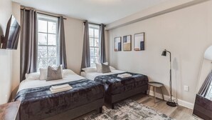 Une chambre d’hôtel moderne avec deux lits, une grande fenêtre, une lampe sur pied et une petite table d’appoint.