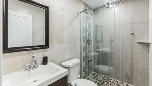 A modern bathroom with a large mirror, a sink, a toilet, and a glass-enclosed shower.