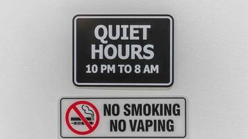 Two signs on a wall: one indicating quiet hours from 10 PM to 8 AM, and another prohibiting smoking and vaping.