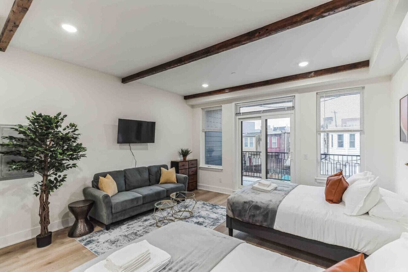 Een moderne woonkamer met een grijze bank, een salontafel, een televisie, een groot raam en een balkon.