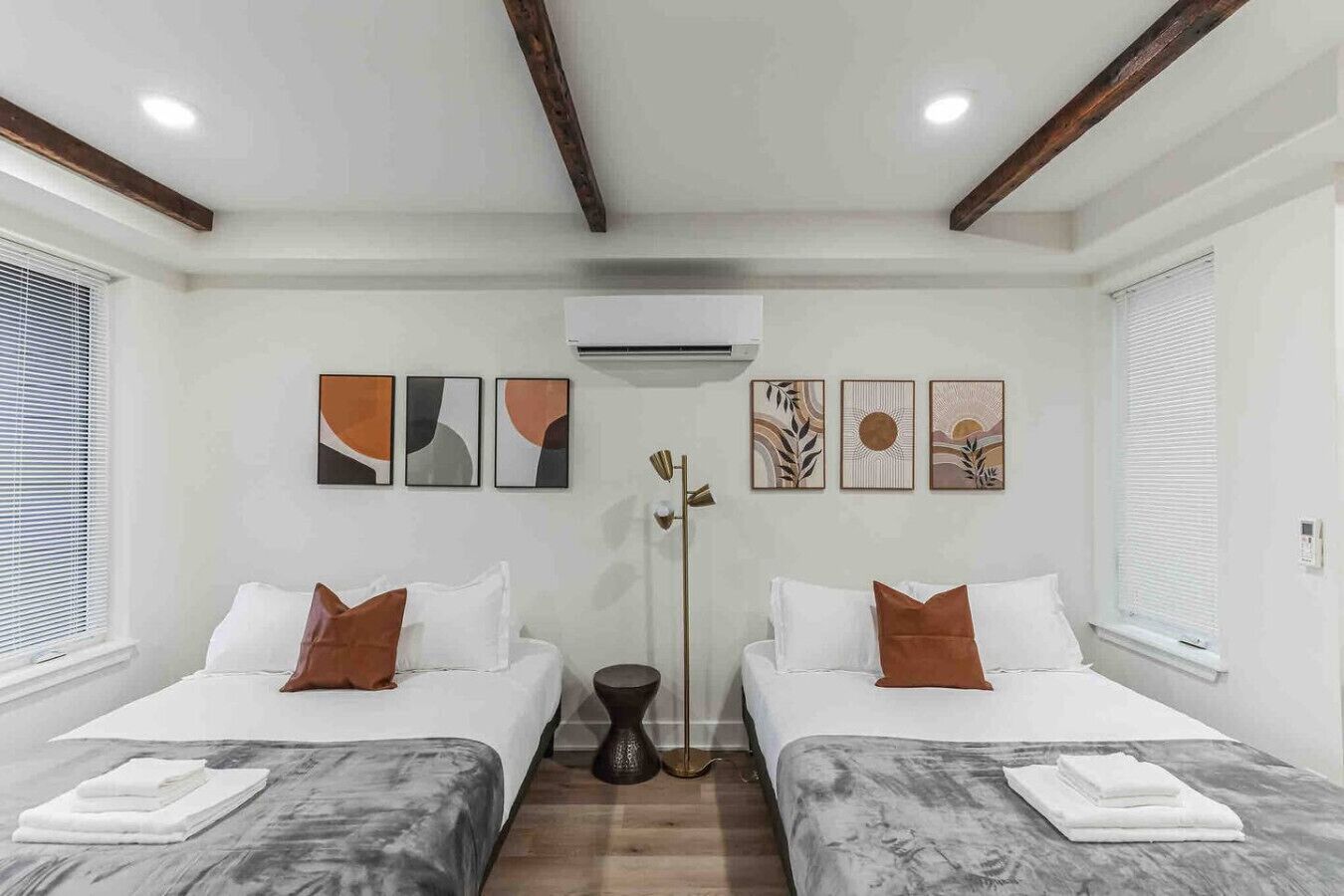 A hotel room with two beds, white bedding, brown pillows, a marble floor, and artwork on the walls.