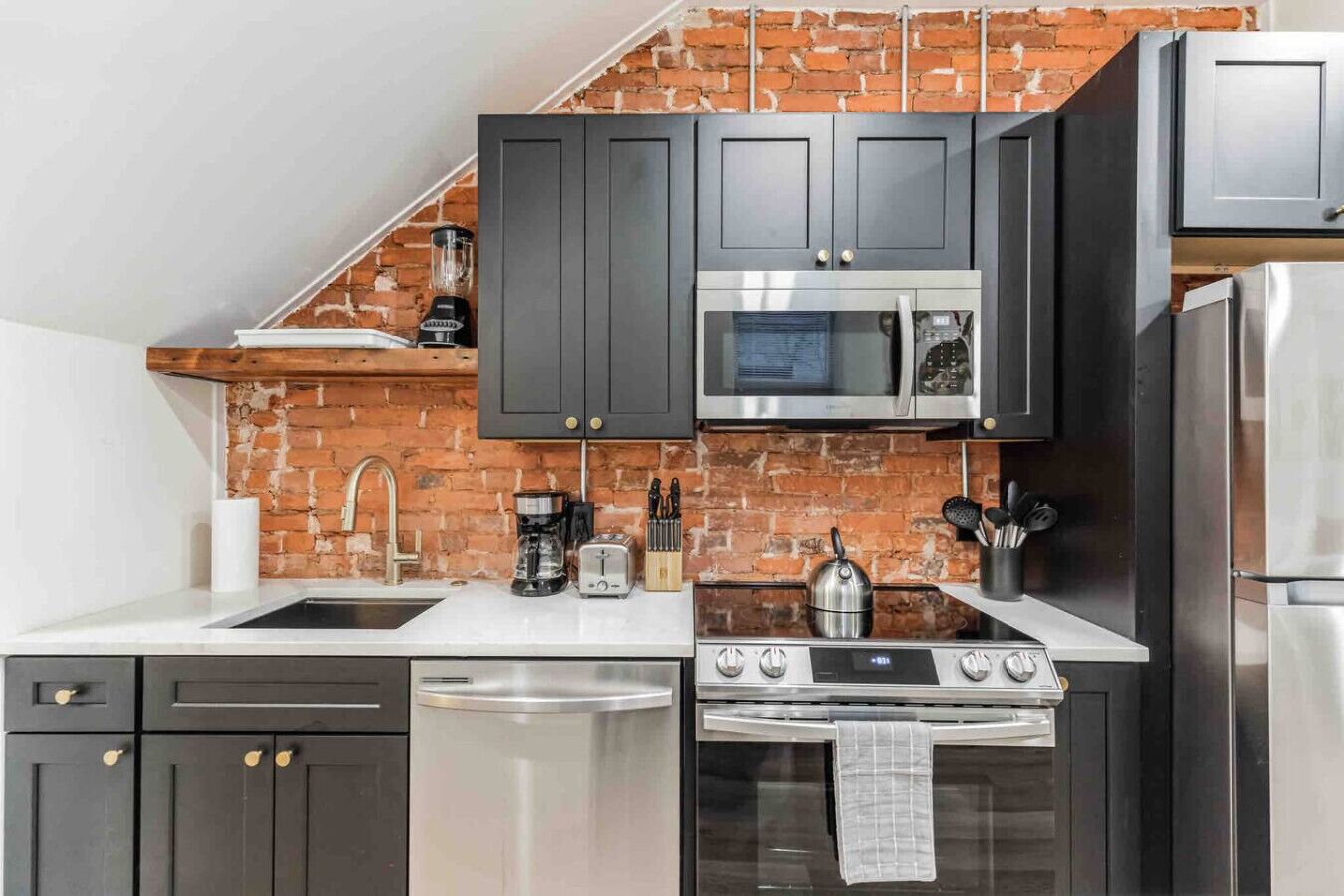A modern kitchen with dark cabinets, a brick backsplash, a stainless steel stove, and a microwave.