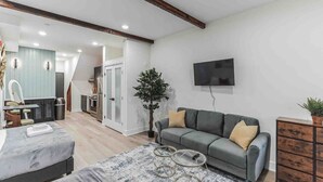 Een moderne woonkamer met een grijze bank, een aan de muur bevestigde televisie en een kleine plant.