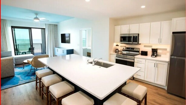 A modern kitchen with white cabinets, a large island with bar stools, a microwave, oven, and refrigerator.