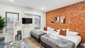 A modern hotel room with two beds, a brick accent wall, a flat-screen TV, and a large window.