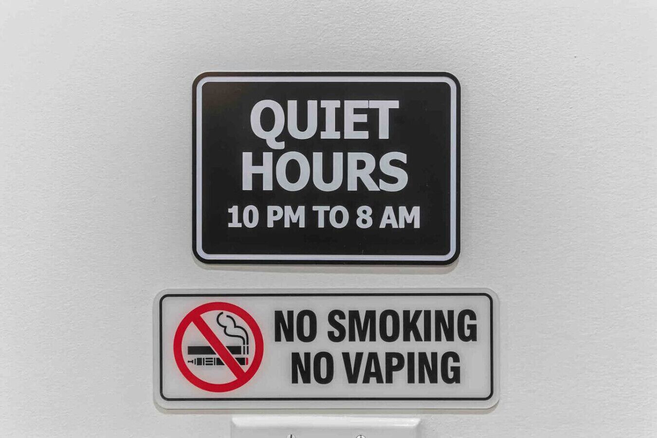 Två skyltar på en vägg: den ena anger att det ska vara tyst mellan klockan 22.00 och 08.00, och den andra förbjuder rökning och användning av e-cigaretter.