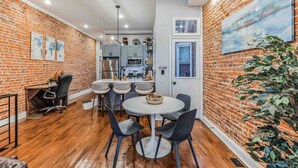 A compact kitchen with modern appliances, a dining area with a round table and chairs, and a brick wall with a large painting. - Large Bi-Level 3/2 w/Patio | 10 min to DT (Philadelphia)