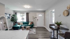 A modern living room with a green sofa, a dining table with chairs, and a white door with a window.