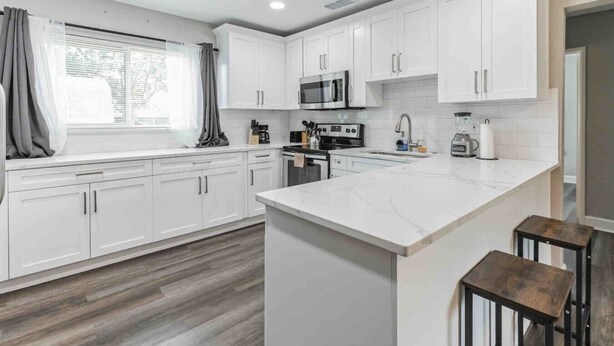 A modern kitchen with white cabinetry, a central island, and a window with curtains.