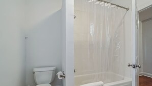 A bathroom with a toilet, a bathtub with a shower curtain, and a wooden floor.