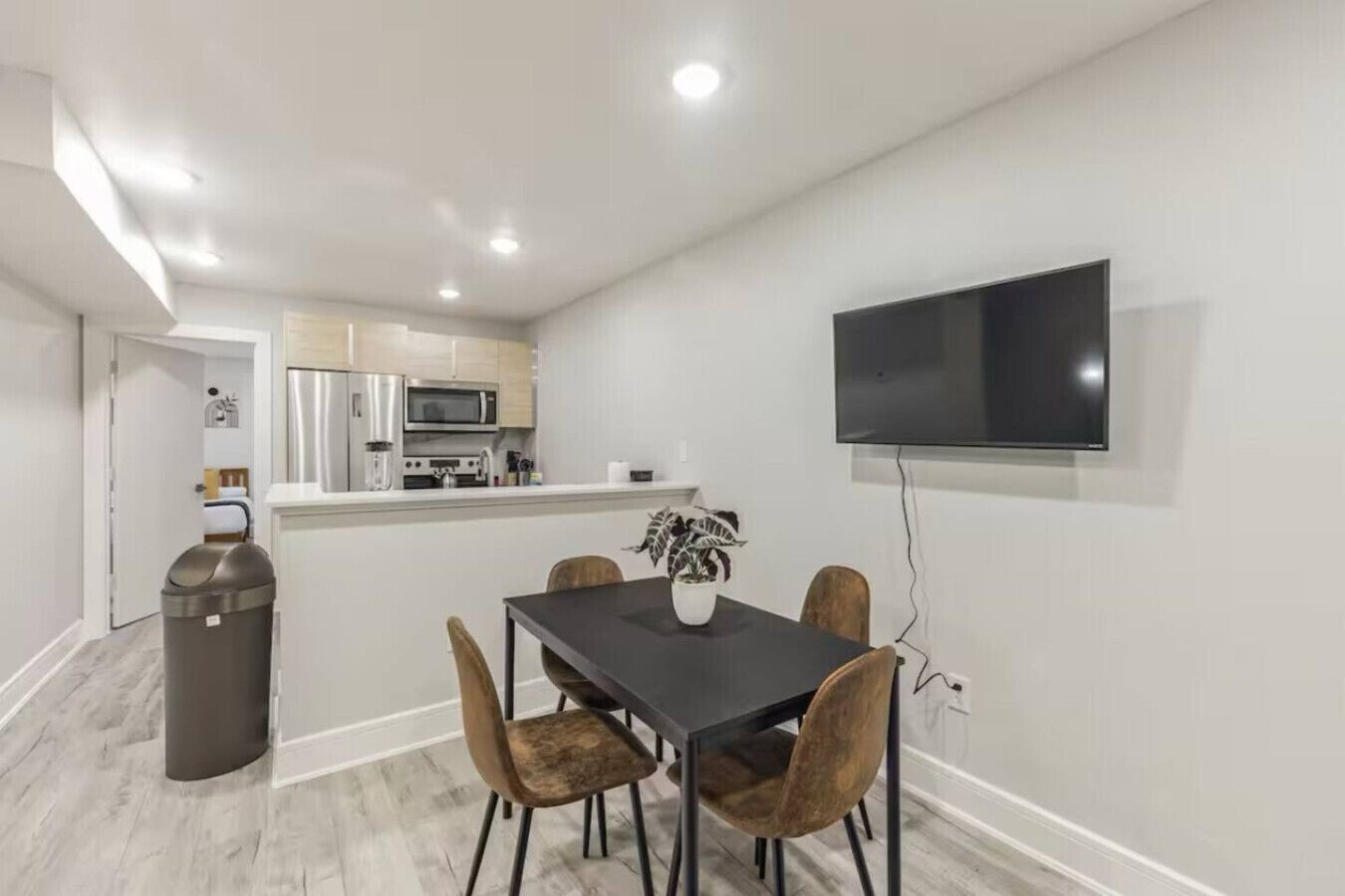 A modern kitchen with stainless steel appliances, a dining area with a table and chairs, and a mounted flat-screen TV.