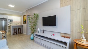 A modern kitchen with a built-in microwave, a large flat-screen TV mounted on the wall, and a dining area with stools. - Beautiful Apartments in the Center of Floripa - CPN (Florianópolis)
