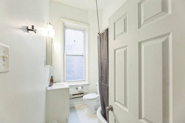 Ein kleines, weißes Badezimmer mit Toilette, Waschbecken und Fenster.