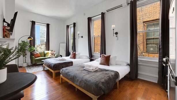 Habitació d'hotel moderna amb dos llits, una zona de seients reduïda, una taula de menjador i grans finestres amb cortines.