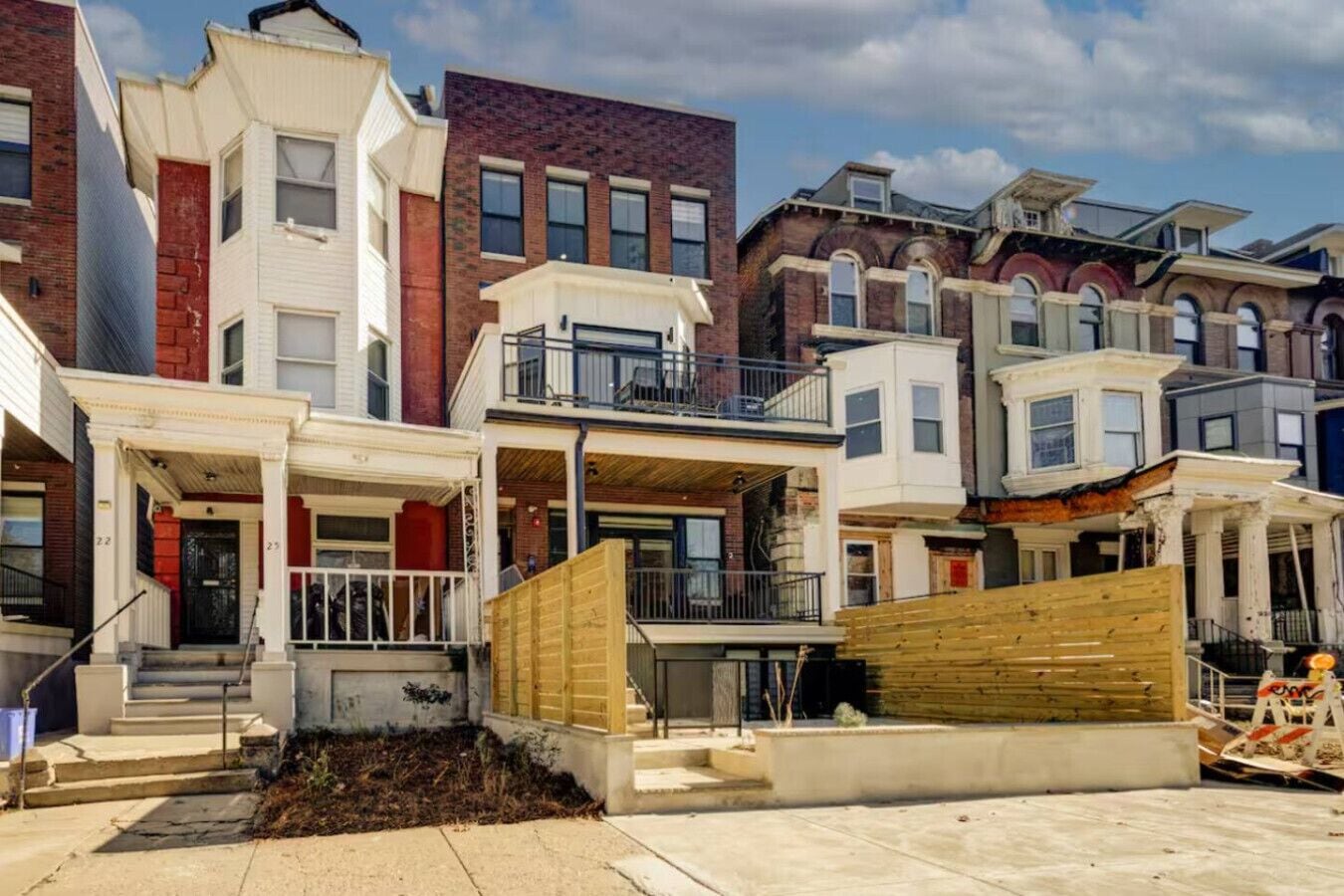 Une rangée de maisons de ville avec des porches à l’avant, une clôture en bois et une barrière de chantier.