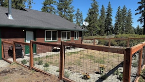 A wooden cabin with a fenced yard, satellite dish, and a garage with a vehicle. - Charming 2-bedroom house private setting with amazing Mt. Shasta view (Weed)