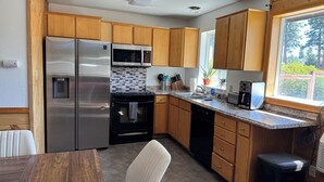 A kitchen with wooden cabinets, stainless steel appliances, and a window with a view of trees. - Charming 2-bedroom house private setting with amazing Mt. Shasta view (Weed)