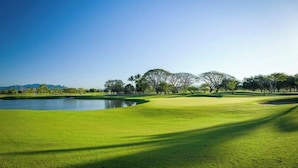 Ein Golfplatz mit Teich, Bäumen und blauem Himmel.