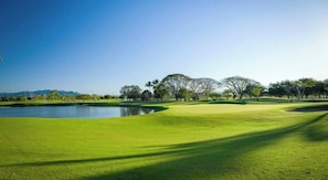 Un parcours de golf avec un étang, des arbres et un ciel dégagé.