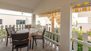 A covered outdoor seating area with a round table and wicker chairs, a white railing, and a view of buildings and greenery. - Cozy apartment in Vir with WiFi (Vir)