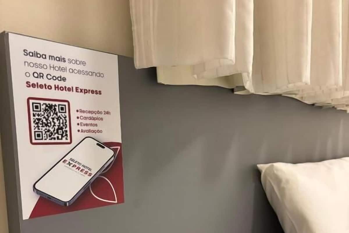 Ett hotellrum med en säng, en kudde och en skylt på väggen som annonserar en QR-kod för Hotel Express-tjänster.