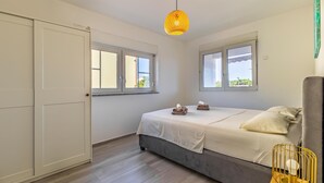 Ein Schlafzimmer mit einem Bett, zwei Fenstern, einem Kleiderschrank und einer Pendelleuchte.