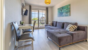 Ein modernes Wohnzimmer mit einem grauen Sofa, einem Esstisch mit Stühlen und einem Hängesessel am Fenster.
